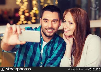 leisure, technology, date, people and holidays concept - happy couple taking selfie by smartphone at restaurant. couple taking selfie by smartphone at restaurant