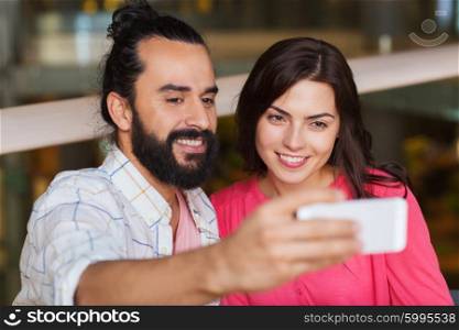 leisure, technology, date, people and holidays concept - happy couple taking selfie by smartphone at restaurant