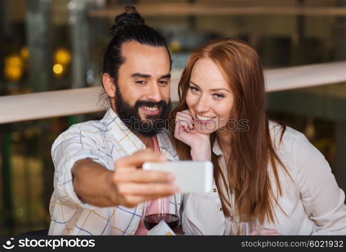 leisure, technology, date, people and holidays concept - happy couple taking selfie by smartphone at restaurant