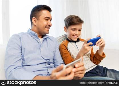 leisure, technology, family and people concept - happy father and son with smartphones at home. happy father and son with smartphones at home