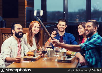 leisure, technology, friendship, people and holidays concept - happy friends having dinner and taking picture by smartphone selfie stick at restaurant. friends taking selfie by smartphone at restaurant. friends taking selfie by smartphone at restaurant