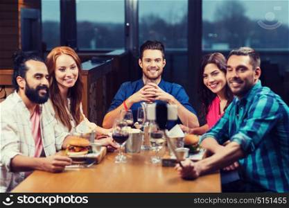 leisure, technology, friendship, people and holidays concept - happy friends having dinner and taking picture by smartphone selfie stick at restaurant. friends taking selfie by smartphone at restaurant