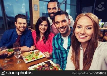 leisure, technology, friendship, people and holidays concept - happy friends having dinner and taking selfie by smartphone at restaurant. friends taking selfie by smartphone at restaurant