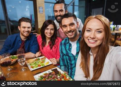 leisure, technology, friendship, people and holidays concept - happy friends having dinner and taking selfie by smartphone at restaurant