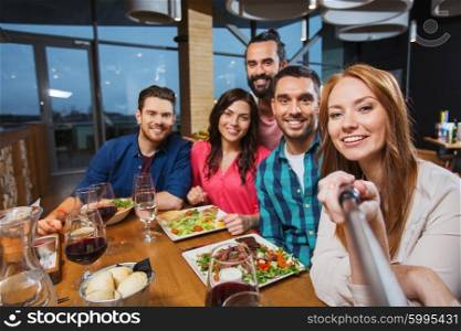 leisure, technology, friendship, people and holidays concept - happy friends having dinner and taking picture by selfie stick at restaurant
