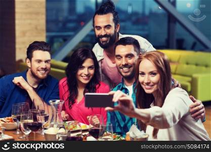 leisure,technology, friendship, people and holidays concept - happy friends having dinner and taking selfie by smartphone at restaurant. friends taking selfie by smartphone at restaurant. friends taking selfie by smartphone at restaurant