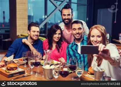 leisure,technology, friendship, people and holidays concept - happy friends having dinner and taking selfie by smartphone at restaurant. friends taking selfie by smartphone at restaurant
