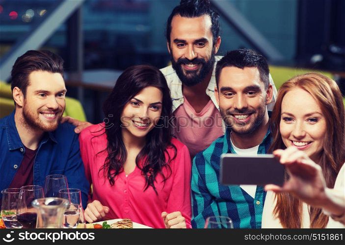 leisure,technology, friendship, people and holidays concept - happy friends having dinner and taking selfie by smartphone at restaurant. friends taking selfie by smartphone at restaurant