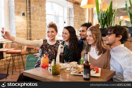 leisure, technology, friendship, people and holidays concept - happy friends with food and drinks taking selfie by smartphone at bar or cafe. friends taking selfie by smartphone at bar or cafe