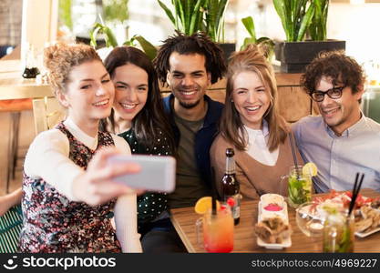 leisure, technology, friendship, people and holidays concept - happy friends with food and drinks taking selfie by smartphone at bar or cafe. friends taking selfie by smartphone at bar or cafe