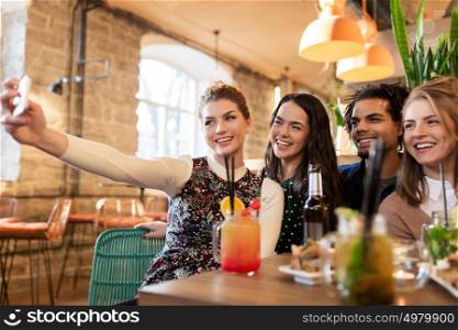 leisure, technology, friendship, people and holidays concept - happy friends with food and drinks taking selfie by smartphone at bar or cafe. friends taking selfie by smartphone at bar or cafe