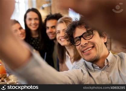leisure, technology, friendship, people and holidays concept - happy man with friends and taking selfie at restaurant. happy man taking selfie with friends at restaurant