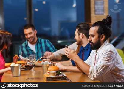 leisure, technology, internet addiction, lifestyle and people concept - man with smartphone and friends at restaurant
