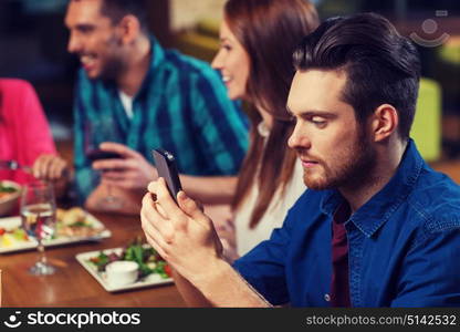 leisure, technology, internet addiction, lifestyle and people concept - man with smartphone and friends at restaurant. man with smartphone and friends at restaurant