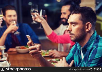 leisure, technology, internet addiction, lifestyle and people concept - man with smartphone and friends at restaurant. man with smartphone and friends at restaurant