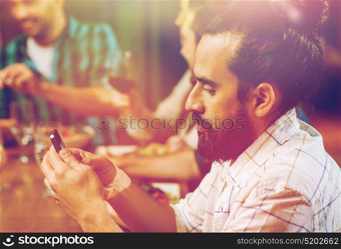 leisure, technology, internet addiction, lifestyle and people concept - man with smartphone and friends at restaurant. man with smartphone and friends at restaurant