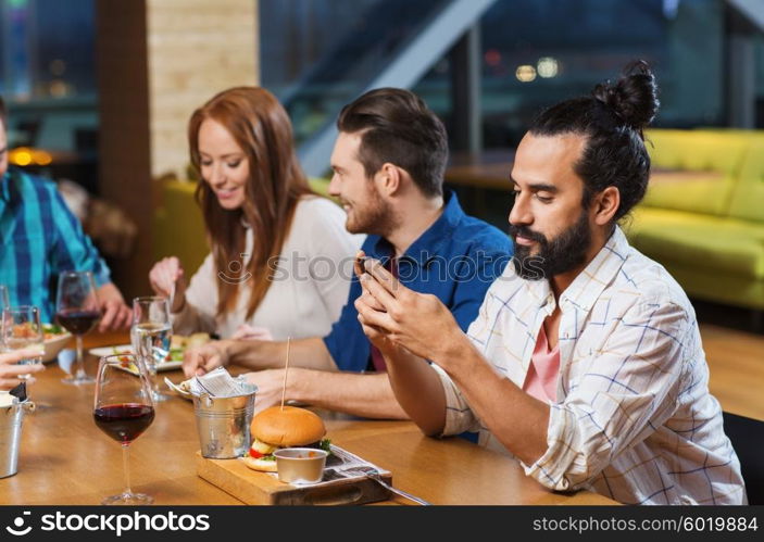 leisure, technology, internet addiction, lifestyle and people concept - man with smartphone and friends at restaurant