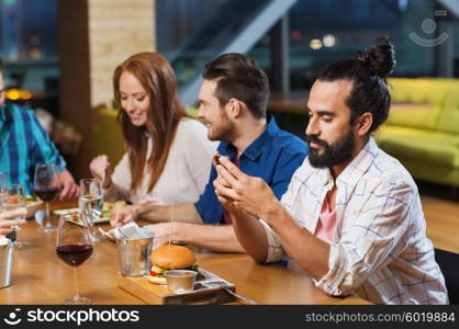 leisure, technology, internet addiction, lifestyle and people concept - man with smartphone and friends at restaurant