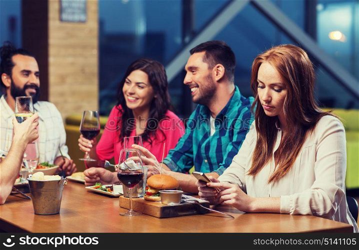 leisure, technology, internet addiction, lifestyle and people concept - woman with smartphone and friends at restaurant. woman with smartphone and friends at restaurant