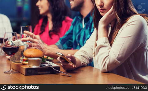 leisure, technology, internet addiction, lifestyle and people concept - woman with smartphone and friends at restaurant. woman with smartphone and friends at restaurant