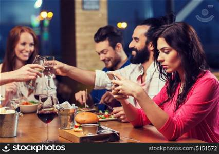 leisure, technology, internet addiction, lifestyle and people concept - woman with smartphone and friends at restaurant. woman with smartphone and friends at restaurant