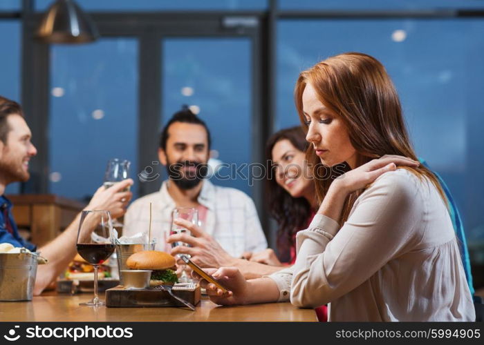 leisure, technology, internet addiction, lifestyle and people concept - woman with smartphone and friends at restaurant