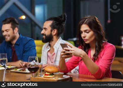 leisure, technology, internet addiction, lifestyle and people concept - woman with smartphone and friends at restaurant