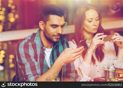 leisure, technology, lifestyle and people concept - couple with smartphones dining at restaurant. couple with smartphones dining at restaurant