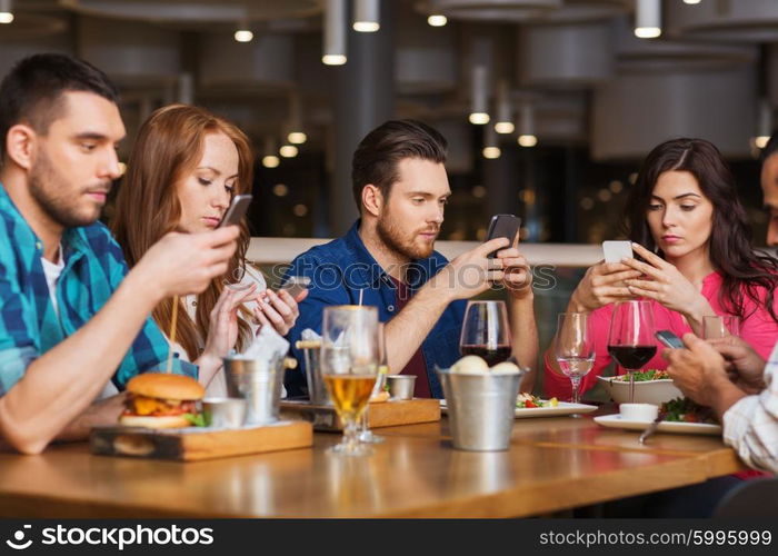 leisure, technology, lifestyle and people concept - friends with smartphones dining at restaurant