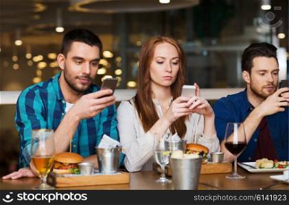 leisure, technology, lifestyle and people concept - friends with smartphones dining at restaurant