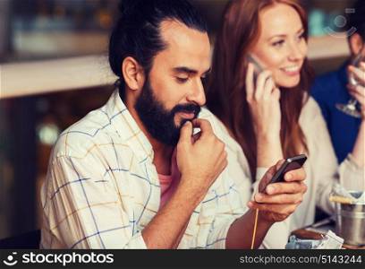leisure, technology, lifestyle and people concept - happy friends with smartphones calling and texting at dinner in restaurant. happy friends with smartphones at restaurant