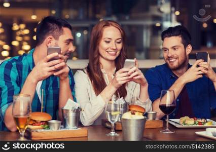 leisure, technology, lifestyle and people concept - happy friends with smartphones dining at restaurant. happy friends with smartphones at restaurant