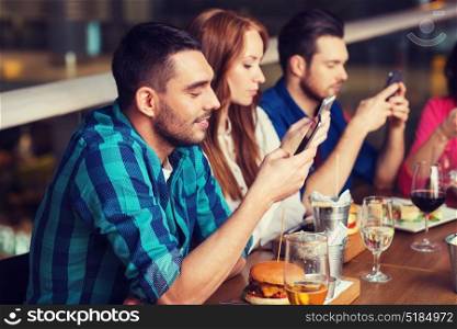 leisure, technology, lifestyle and people concept - happy friends with smartphones dining at restaurant. friends with smartphones dining at restaurant