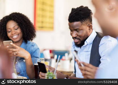 leisure, technology, lifestyle and people concept - happy friends with smartphones dining at restaurant. happy friends with smartphones at restaurant