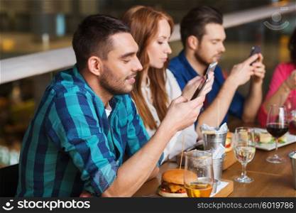 leisure, technology, lifestyle and people concept - happy friends with smartphones dining at restaurant