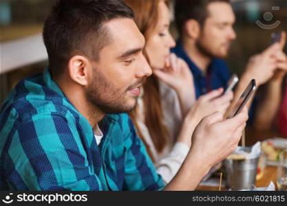 leisure, technology, lifestyle and people concept - happy friends with smartphones dining at restaurant