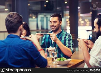 leisure, technology, lifestyle and people concept - happy friends with smartphones taking picture of food at restaurant. happy friends taking picture of food at restaurant