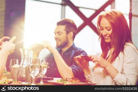 leisure, technology, lifestyle and people concept - happy friends with smartphones taking picture of food at restaurant. happy friends taking picture of food at restaurant