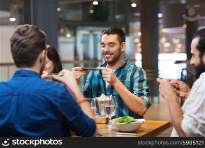 leisure, technology, lifestyle and people concept - happy friends with smartphones taking picture of food at restaurant