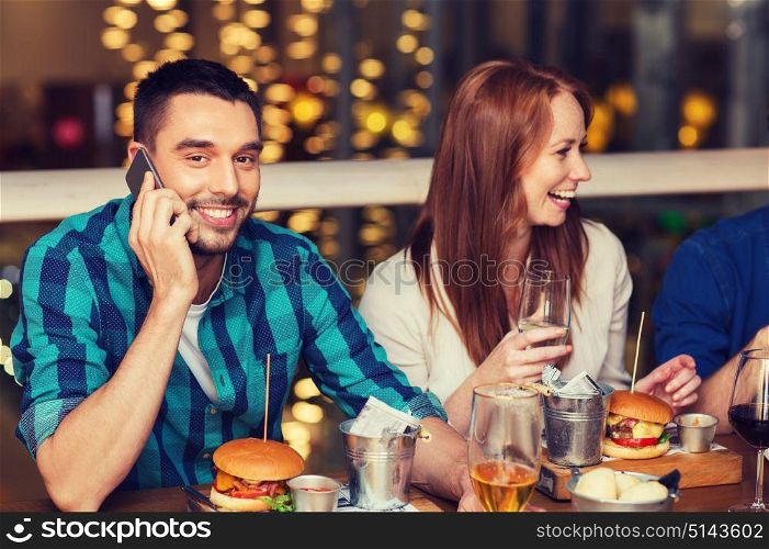 leisure, technology, lifestyle and people concept - happy man with smartphone and friends dining at restaurant. man with smartphone and friends at restaurant