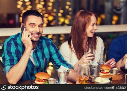 leisure, technology, lifestyle and people concept - happy man with smartphone and friends dining at restaurant. man with smartphone and friends at restaurant