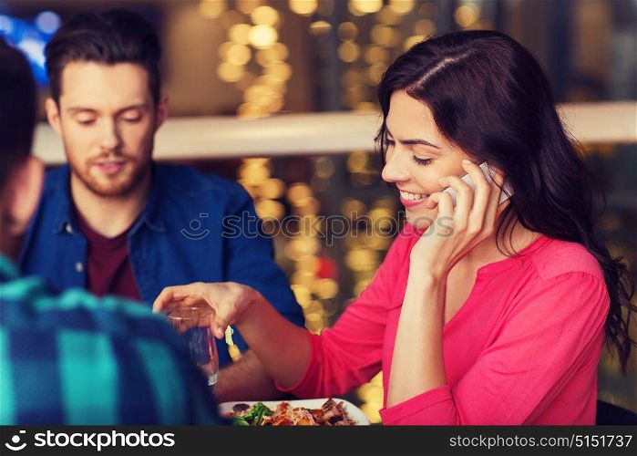 leisure, technology, lifestyle and people concept - happy woman calling on smartphone and dining at restaurant with friends. woman with smartphone and friends at restaurant