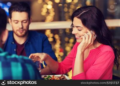 leisure, technology, lifestyle and people concept - happy woman calling on smartphone and dining at restaurant with friends. woman with smartphone and friends at restaurant
