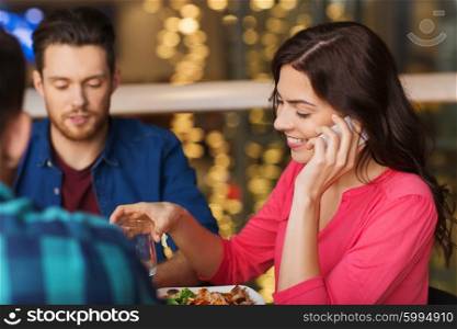 leisure, technology, lifestyle and people concept - happy woman calling on smartphone and dining at restaurant with friends