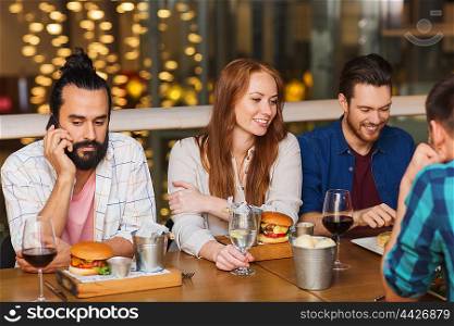 leisure, technology, lifestyle and people concept - man with smartphone and friends dining at restaurant