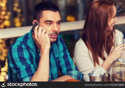 leisure, technology, lifestyle and people concept - man with smartphone and friends dining at restaurant. man with smartphone and friends at restaurant