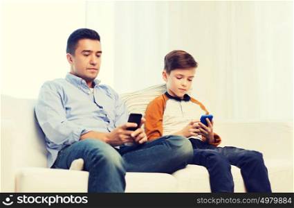 leisure, technology, technology, family and people concept - father and son with smartphones texting message or playing game at home. father and son with smartphones at home