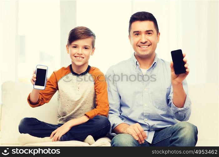 leisure, technology, technology, family and people concept - happy father and son showing smartphone blank screens at home. happy father and son with smartphones at home