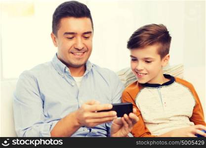 leisure, technology, technology, family and people concept - happy father and son with smartphone texting message or playing game at home. happy father and son with smartphone at home