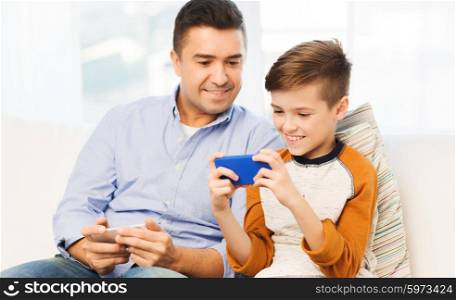leisure, technology, technology, family and people concept - happy father and son with smartphone texting message or playing game at home